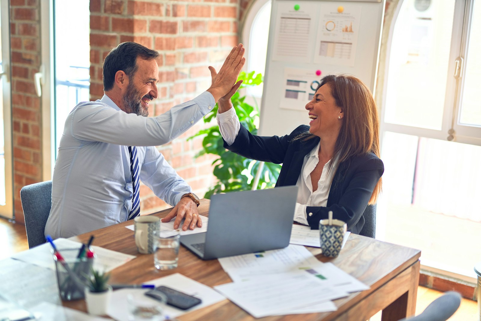 Two business partners celebrating with a high five at their laptop